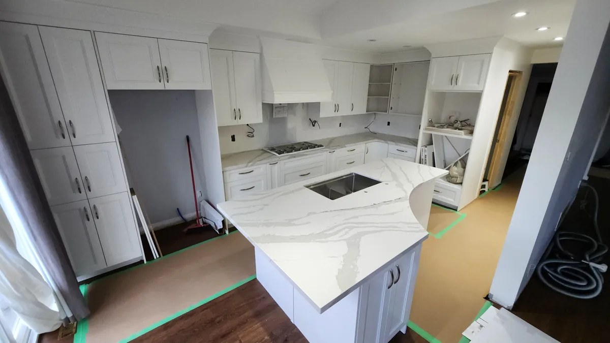Finished kitchen with a quartz waterfall island and white shaker cabinets